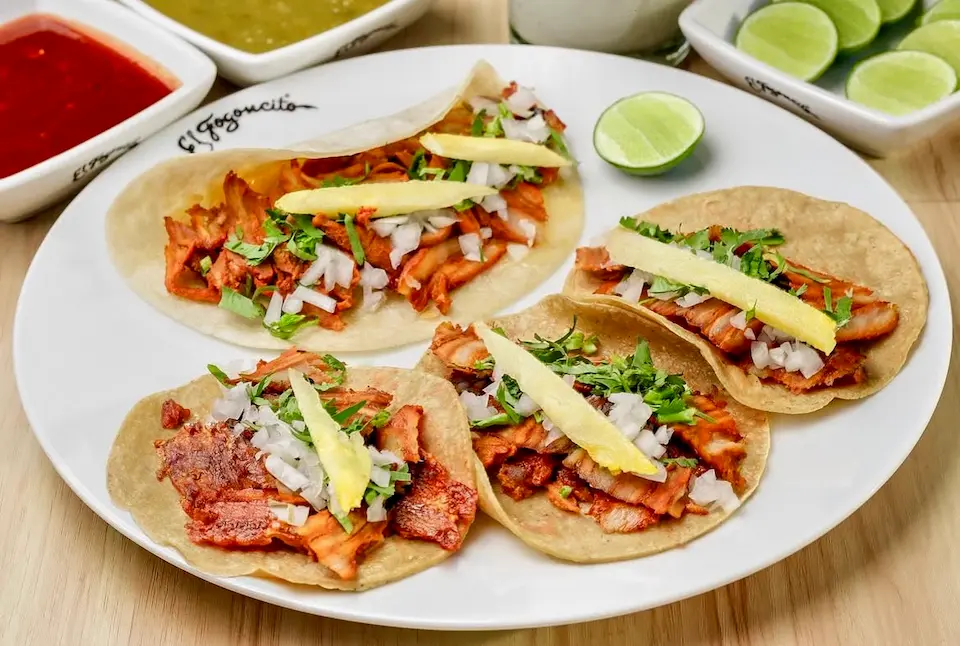 Un trompo de carne al pastor recién cortada, con piña asada, tortillas calientes, cilantro, cebolla y salsa mexicana.